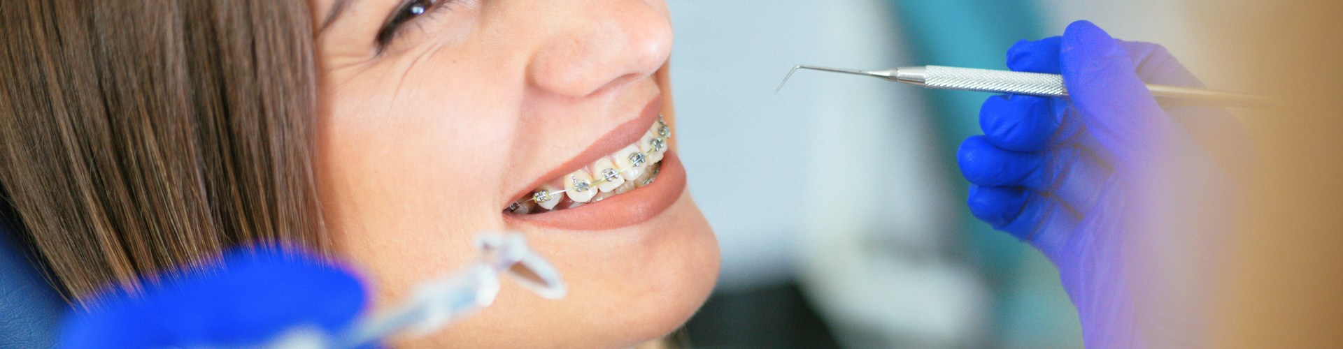 Gloved hands holding dental tools around woman's smile with metal braces.